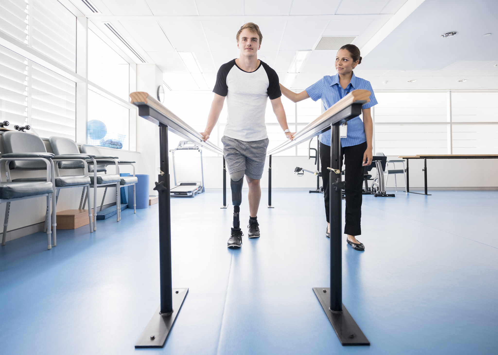Man with prosthetic leg using parallel bars with physyiotherapist